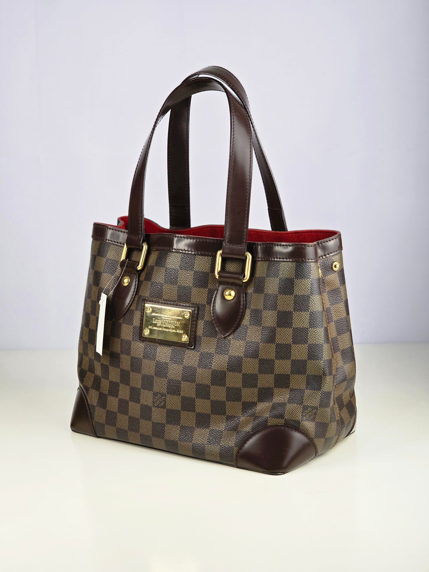 Designer brown checkered handbag with leather handles and gold hardware on a light surface.